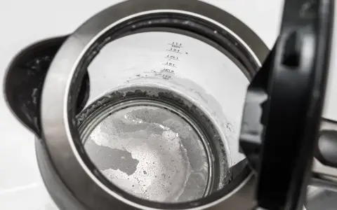 Widok wnętrza czajnika z widocznym kamieniem, który wymaga odkamienienia. Widać osad na dnie i ściankach.