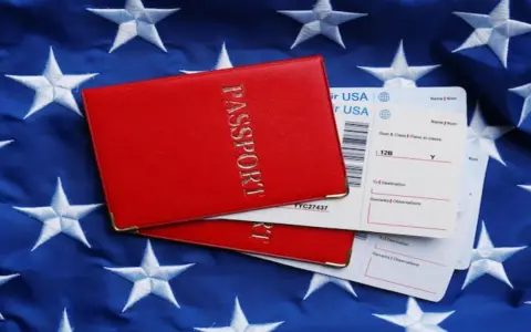 Czerwony paszport i bilety lotnicze na tle flagi USA. Zastanawiasz się, ile kosztuje bilet do USA w dwie strony?