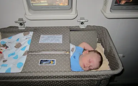 Śpiące dziecko w wózku dla dziecka Singapore Airlines podczas lotu. Wygodny enter air wózek dla dziecka zapewnia spokojny sen maluchowi.
