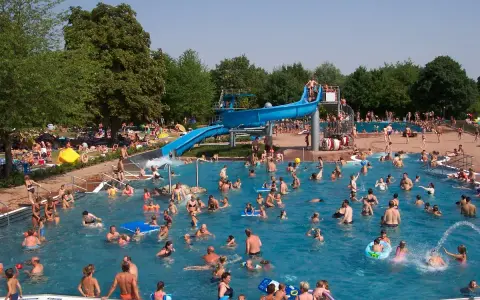 Ein belebtes Freibad in Goslar mit vielen Menschen, die im Wasser planschen und die blaue Wasserrutsche genießen.