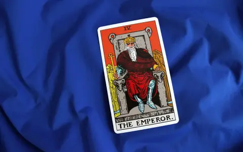 Karta cesarz tarot, przedstawiająca władcę na tronie, leży na niebieskim tle.