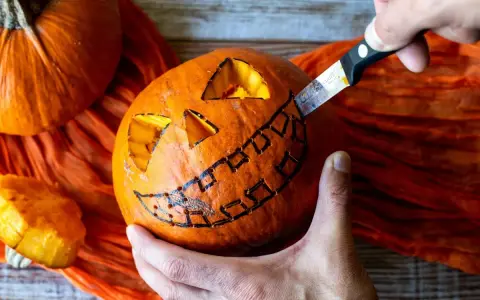 Creando una calabaza de Halloween fácil. Un cuchillo talla una sonrisa dentada en una calabaza naranja, con ojos triangulares ya cortados.