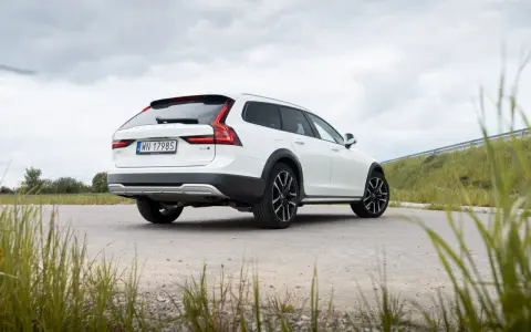 Białe Volvo Cross Country na tle pochmurnego nieba i zielonych wzgórz.