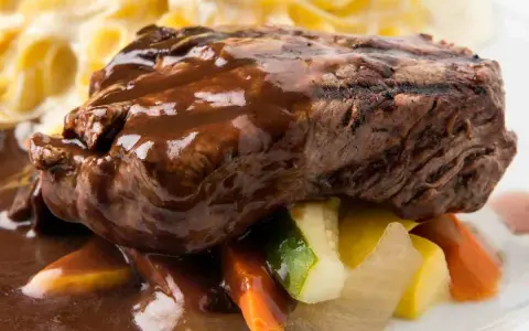 Succulento brasato di manzo nappato con salsa scura, servito su verdure miste e accompagnato da pasta.