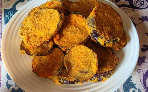 Fette dorate di melanzane in friggitrice ad aria, impanate e croccanti, servite su un piatto bianco.