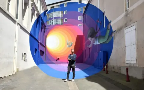 Un artiste street art français pose devant sa fresque colorée d'une fillette et d'un lapin flottant dans un tunnel psychédélique.