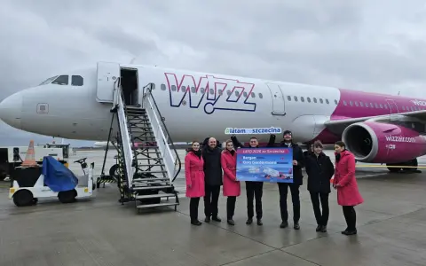 Grupa osób pozuje przed samolotem Wizz Air, trzymając tablicę z informacją o nowych trasach, w tym lotach Szczecin-Bergen.