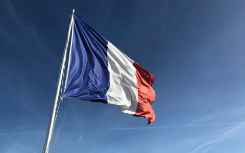 Flaga Francji powiewa na maszcie na tle błękitnego nieba z smugami chmur.