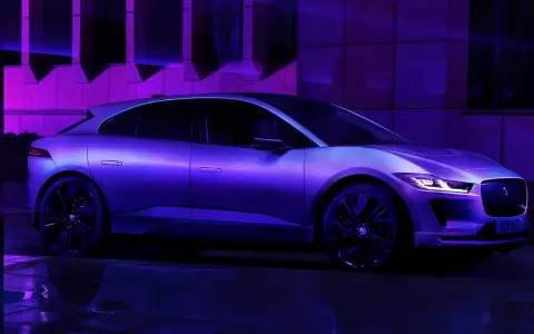 Jaguar I-Pace w fioletowym świetle, zaparkowany na mokrej nawierzchni.