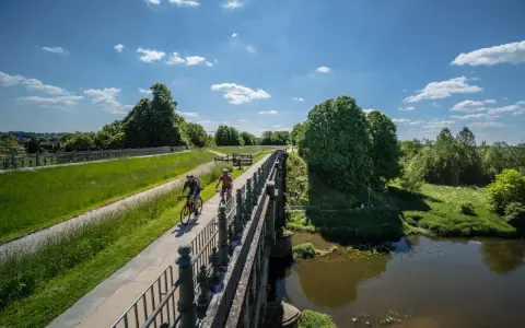 Zwei Radfahrer genießen die Aussicht auf der hohen Mark Radroute über eine Brücke, umgeben von grünen Wiesen und Bäumen.