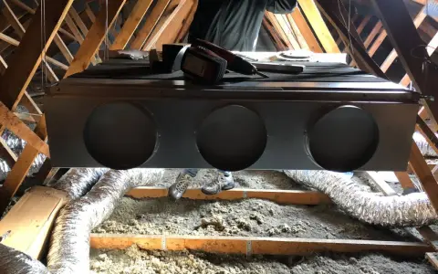 Installation d'un système de climatisation gainable dans un grenier. Un technicien est visible, prêt pour l'entretien.