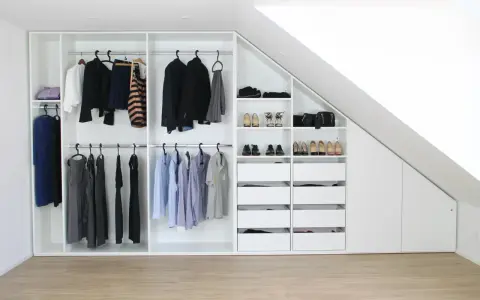 Einbauschrank selber bauen: Weißer Schrank mit Kleiderstangen, Schubladen und Schuhfächern unter einer Dachschräge.