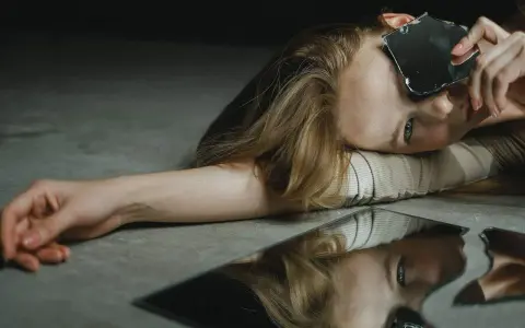 Une femme aux cheveux blonds, le visage tourné, tient un éclat de miroir. Son reflet brisé sur le sol évoque le narcissique et les femmes.