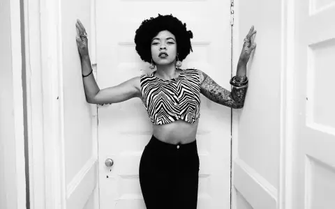 Nikki Hill, con su afro y top de cebra, posa con confianza entre puertas blancas.