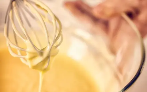 Frusta da cucina che raccoglie una densa pastella per fritti, pronta per creare delizie croccanti.