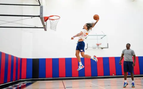 Un joueur de basket-ball en plein saut, ballon en main, effectue un exercice de pliométrie. Un autre joueur observe.