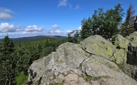 Kamienne formacje na rozdrożu izerskim, porośnięte mchem, z widokiem na gęsty las i błękitne niebo z chmurami.