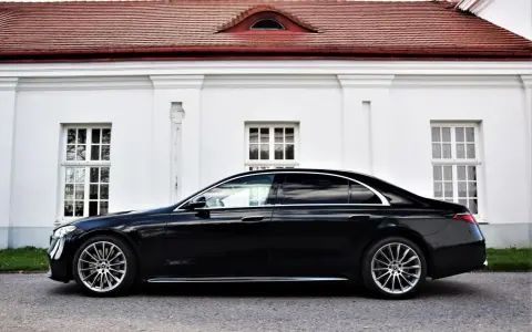 Elegancki, czarny Mercedes S500 lśni na tle białej, zabytkowej fasady z czerwonym dachem.