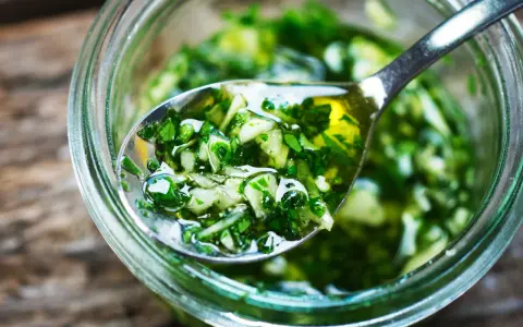 Łyżka z aromatycznym, zielonym sosem chimichurri, pełnym ziół i czosnku, zanurzona w słoiku.