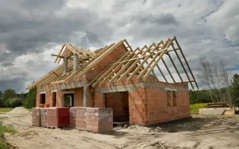 Budowa domu 220m2 w stanie surowym. Ceglane ściany, drewniany dach, materiały budowlane na placu.