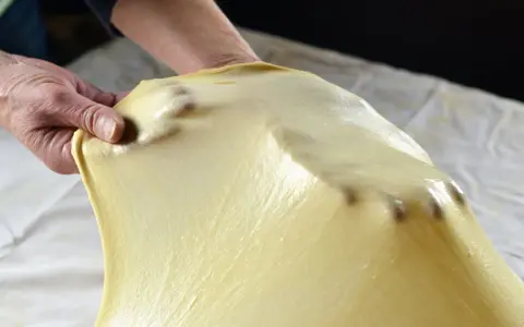 Mani che stendono la pasta matta per una ricetta tradizionale. La pasta è sottile e traslucida, con le dita che creano delle leggere ondulazioni.