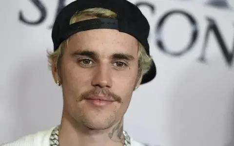 Justin Bieber con un gorra negra y un bigote herradura, luciendo una cadena plateada.