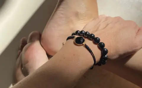 Pulsera con cuentas de obsidiana, una piedra negra protectora, junto a unos pies.