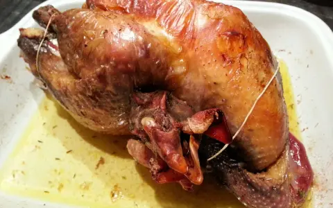 Une pintade au four, dorée et juteuse, repose dans un plat blanc, baignant dans son jus savoureux.