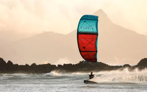 Kitesurfer na desce w akcji, z kolorowym latawcem na tle gór i morza.