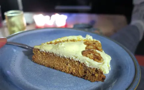 En bit saftig glutenfri morotskaka med krämig frosting och valnötter på en blå tallrik.