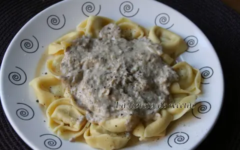 Tortellini de queso cubiertos con una cremosa salsa de champiñones y pimienta negra, servidos en un plato blanco con espirales decorativas.