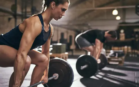 Kvinna fokuserar på ett helkroppspass 3 gånger i veckan, redo att lyfta skivstången i gymmet.