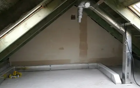 Na poddaszu widać system rur wentylacyjnych, biegnących wzdłuż drewnianej konstrukcji dachu i wzdłuż ściany.