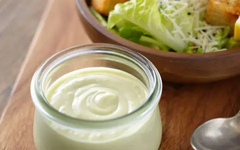 Cremiges Dressing in einem Glas, bereit für einen köstlichen veganen Caesar Salad mit Croutons und Parmesan-Alternative.