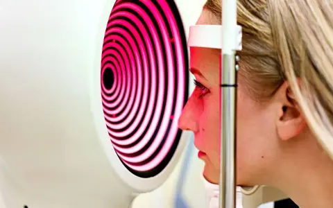 Esame oculistico: una donna guarda un dispositivo che proietta una mappa corneale a spirale rosa e nera.