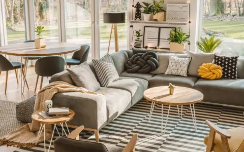 Un salón moderno y acogedor con sofá gris, alfombra de rayas, mesa de centro de madera y grandes ventanales que dejan entrar la luz natural.