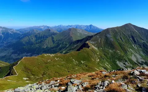 Widok na pasmo górskie z wyraźną ścieżką wijącą się po zboczu. W oddali widać kolejne szczyty Tatr, w tym Starorobociański Wierch.