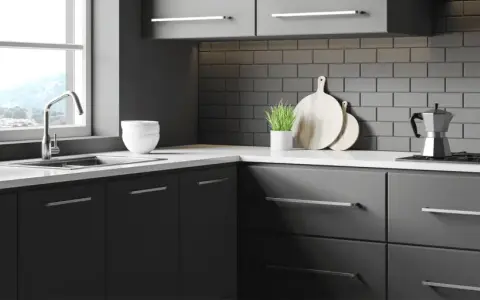 Une cuisine moderne et épurée, idéale pour rénover sa cuisine sans changer les meubles. Des placards sombres, un plan de travail blanc et un crédence en briques grises.