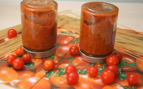 Zwei Schraubgläser mit selbstgemachter Tomatensauce, umgeben von frischen Tomaten und Spaghetti. Perfekt zum Tomatensauce einkochen.