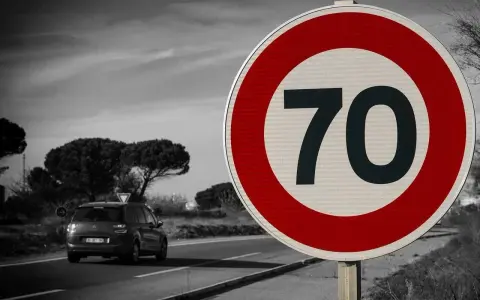 Znak drogowy ograniczający prędkość do 70 km/h, samochód na drodze.