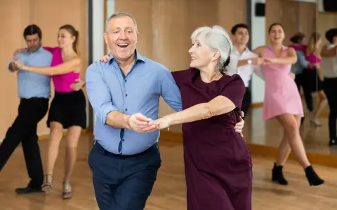Uśmiechnięta para seniorów uczy się, jak tańczyć na 3, w tle inne pary.