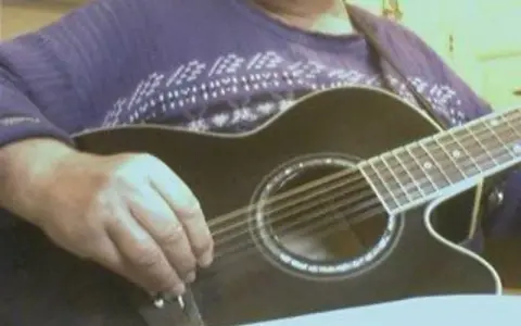 Main d'un musicien ajustant l'accordage 12 cordes d'une guitare acoustique noire.