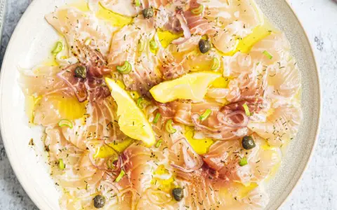 Délicieux carpaccio de saumon, fines tranches de poisson cru arrosées d'huile d'olive, garnies de câpres, oignons rouges et quartiers de citron.