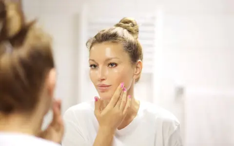 Donna con capelli raccolti applica un siero sul viso. La domanda è: quanti sieri si possono usare insieme per una pelle luminosa?