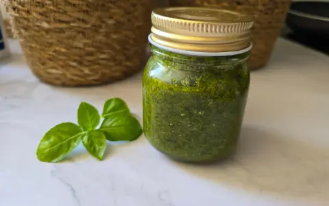 Un pot de pesto maison, vert vif, à côté de feuilles de basilic frais. Parfait pour sublimer vos plats !