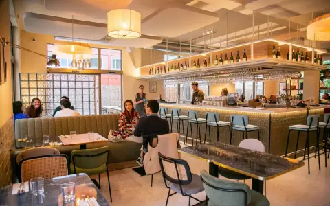 Ambiance chaleureuse d'un restaurant, avec des clients attablés et un bar bien garni. L'esprit du terroir se retrouve dans la sélection des vins et la convivialité.