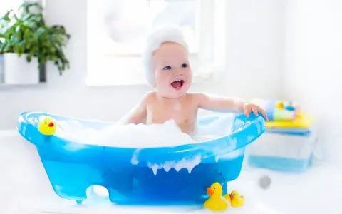 Radosna kąpiel noworodka w pianie, z gumowymi kaczuszkami. Uśmiechnięte dziecko w niebieskiej wanience.