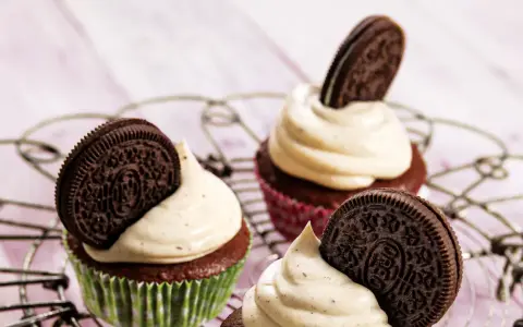 Drei leckere Oreo Muffins mit cremiger Glasur und einem ganzen Oreo-Keks darauf, auf einem Gitter.
