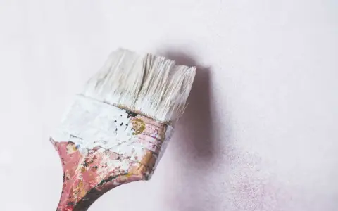 Pincel desgastado con restos de pintura blanca a punto de tocar una pared de cal con textura sutil.