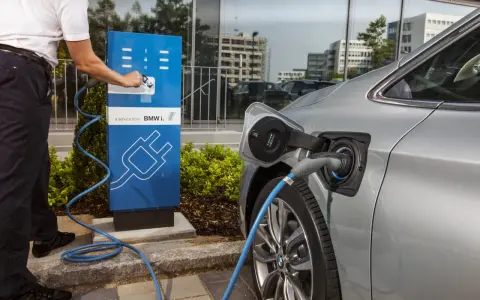 Un uomo collega un'auto elettrica a una colonnina di ricarica BMW i. Un passo verso il calcolo risparmio auto elettrica.